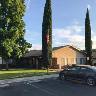 A sunny outdoor scene featuring a residential building, tall trees, and an American flag.