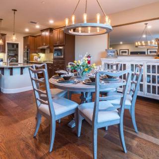 A beautifully designed open-concept dining area with a round table, elegant chandelier, and view into the kitchen.