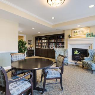 A cozy library with a round table, chairs, and a fireplace surrounded by bookshelves.