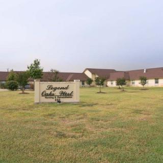 A residential building with a sign reading 'Raymond Cedar Wind' on a grassy lawn under a cloudy sky.