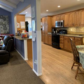 The image shows an open-concept kitchen and living room with wooden cabinets and a dining table.