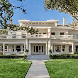 A grand colonial-style mansion with a spacious porch and well-manicured lawn.