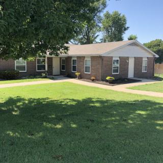 A suburban brick house with a well-maintained lawn and large tree.