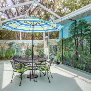 A bright patio with a table, chairs, and a colorful umbrella set against a mural backdrop.