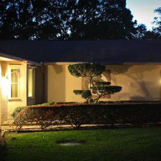 A beautifully lit house at night, showcasing a well-maintained garden and lush landscaping.
