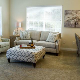 A cozy living room with a sofa, armchair, and patterned ottoman, featuring soft lighting and elegant decor.