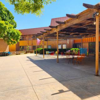 A sunny outdoor courtyard featuring a patio area with seating and surrounding greenery.