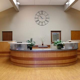 A modern office reception area with a central desk, decorative plants, and a large wall clock.