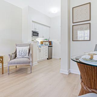 A modern open-plan living space featuring a cozy armchair, dining table, and a compact kitchen with white cabinetry.