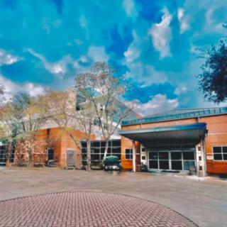 A brick building with a modern entrance under a vivid, partly cloudy sky.