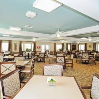 A spacious dining room with neatly arranged tables and chairs, featuring ceiling fans and soft lighting.