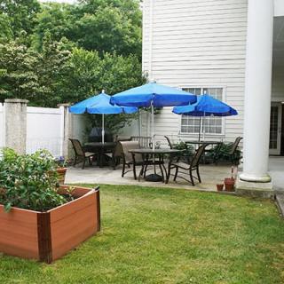 A cozy backyard patio with blue umbrellas and a small garden area.
