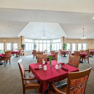 A spacious dining room with tables covered in red tablecloths, surrounded by wooden chairs and large windows.