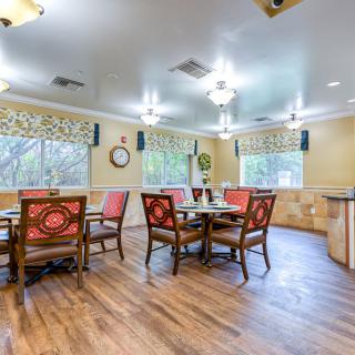 A bright dining area with wooden floors, tables, and chairs, illuminated by ceiling lights.