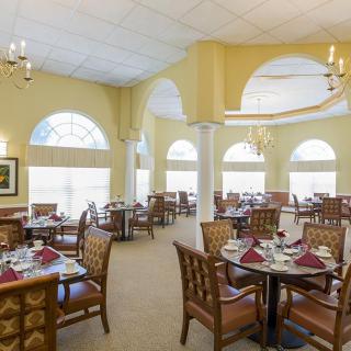 An elegant dining area with neatly arranged tables and chairs, featuring chandeliers and arched windows.