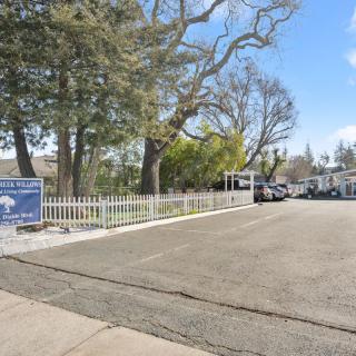 A parking lot surrounded by trees and a fence, with several cars parked during the daytime.