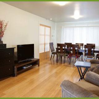 A spacious living room with a connected dining area, featuring a television, sofa, and dining table on hardwood flooring.