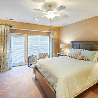 A cozy bedroom with a large bed, ceiling fan, and natural light filtering through the curtains.
