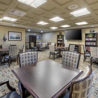 An inviting communal room with tables and chairs, featuring a large television and library shelves.