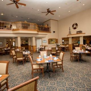 A spacious restaurant dining area with tables and chairs, featuring ceiling fans and a carpeted floor.