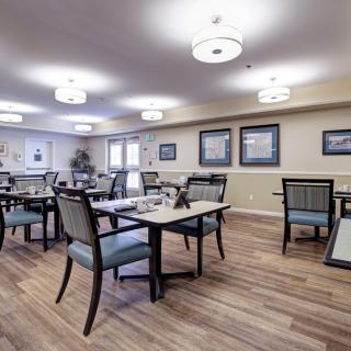 A modern dining room with neatly arranged tables and chairs, featuring warm lighting and wooden flooring.