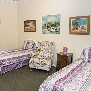 A cozy bedroom with twin beds, a floral chair, and wall art.