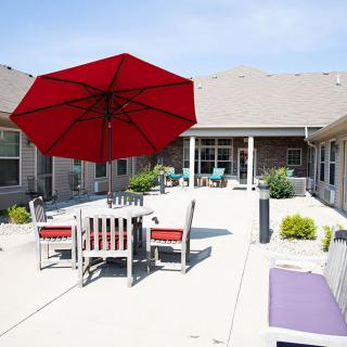 A sunny patio with a red umbrella and outdoor seating area.