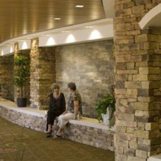 Two people sitting and conversing in a modern lobby with stone walls and potted plants.