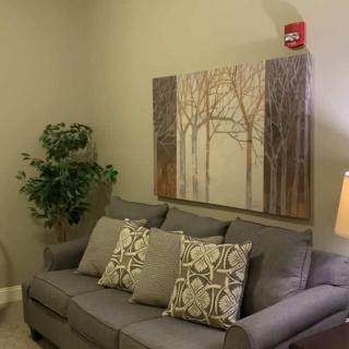A cozy living room with a gray sofa, decorative cushions, and a nature-themed painting on the wall.