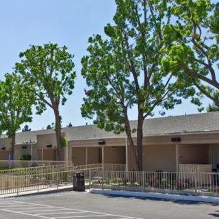 A view of a building with trees and a parking lot in the foreground.