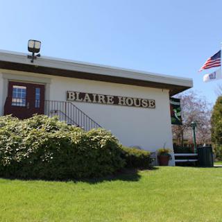 The exterior view of a building with a sign reading 'HEARSE HOUSE' and an American flag waving in front.