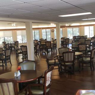 An empty dining area with multiple tables and chairs, featuring a wooden floor and natural lighting.