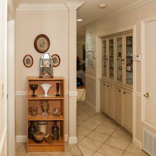 A cozy hallway featuring a wooden shelf adorned with decorative ceramics and frames, leading to a built-in cabinet along the wall.