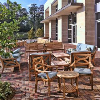 A modern outdoor patio area featuring wooden furniture and surrounded by greenery.