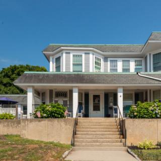 A two-story house featuring a welcoming porch and front steps, surrounded by greenery.