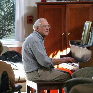 A man playing the piano indoors with sunlight streaming in.