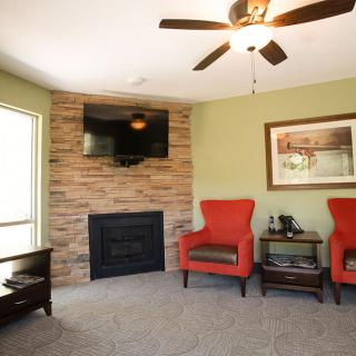 A cozy living room with red armchairs, a brick fireplace, and a mounted television.