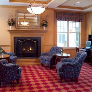A cozy lobby area featuring armchairs around a fireplace with a decorative carpet.