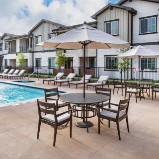 A sunny outdoor pool area with lounge chairs, tables, and umbrellas in a resort setting.