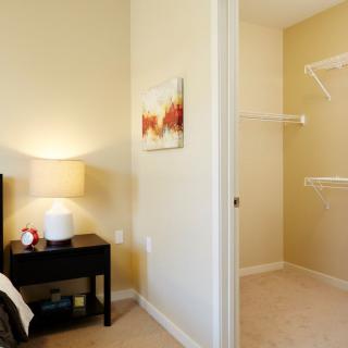 A cozy bedroom with a nightstand and lamp, featuring a small closet.
