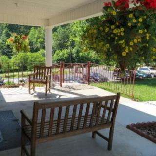 A peaceful porch with wooden benches and hanging plants overlooking a garden.