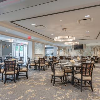A spacious and elegantly decorated dining room with multiple tables and chairs, featuring modern chandeliers.