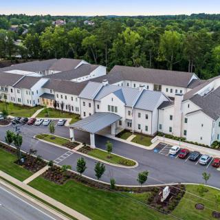Aerial view of a large building complex surrounded by trees and a parking area.