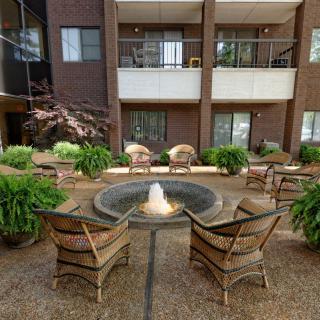 A cozy outdoor seating area with a central fountain surrounded by greenery, in front of an apartment building.