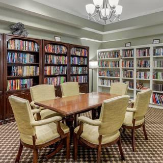 A cozy library room with bookshelves, a wooden table, and comfortable chairs.