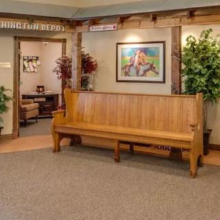 A cozy waiting area with a wooden bench, artwork on the wall, and indoor plants.