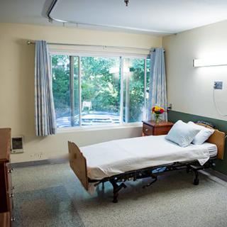 A hospital room with a bed near a large window letting in sunlight.