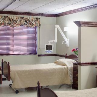 A hospital room with a single bed, curtains, and a wall-mounted monitor.