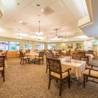 A spacious and elegant dining area with neatly arranged tables and chairs, illuminated by ceiling lights.