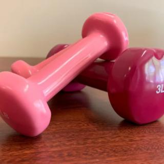 A pair of pink dumbbells resting on a wooden surface.